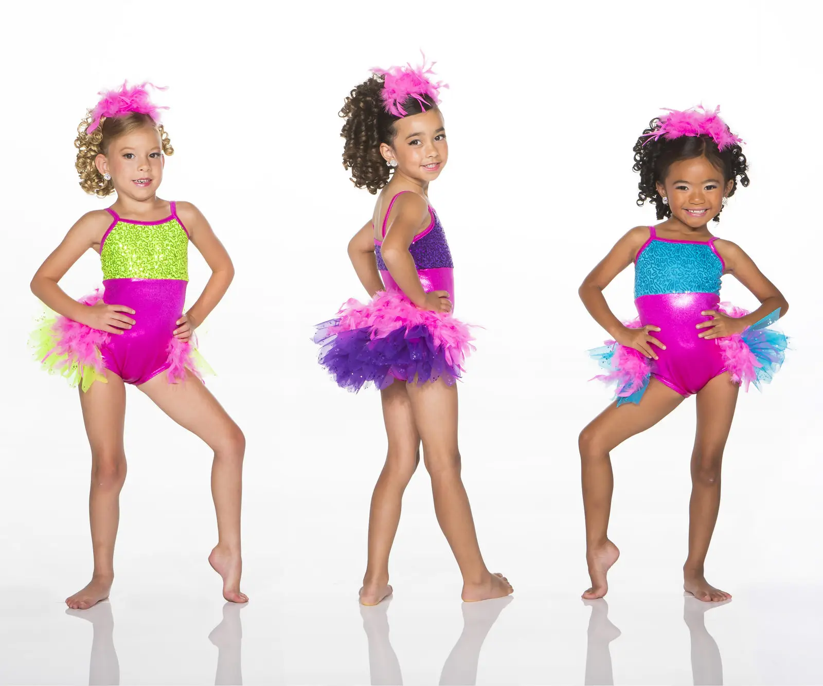 Three young dancers in colorful sequined costumes and feathered skirts