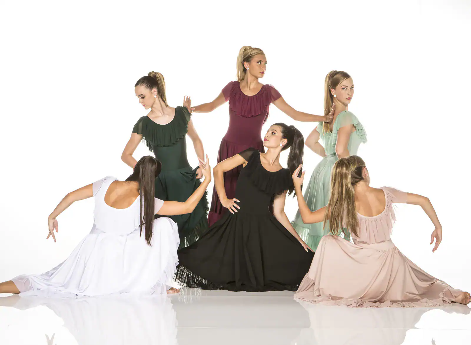 Six women pose in flowing ruffled dresses.