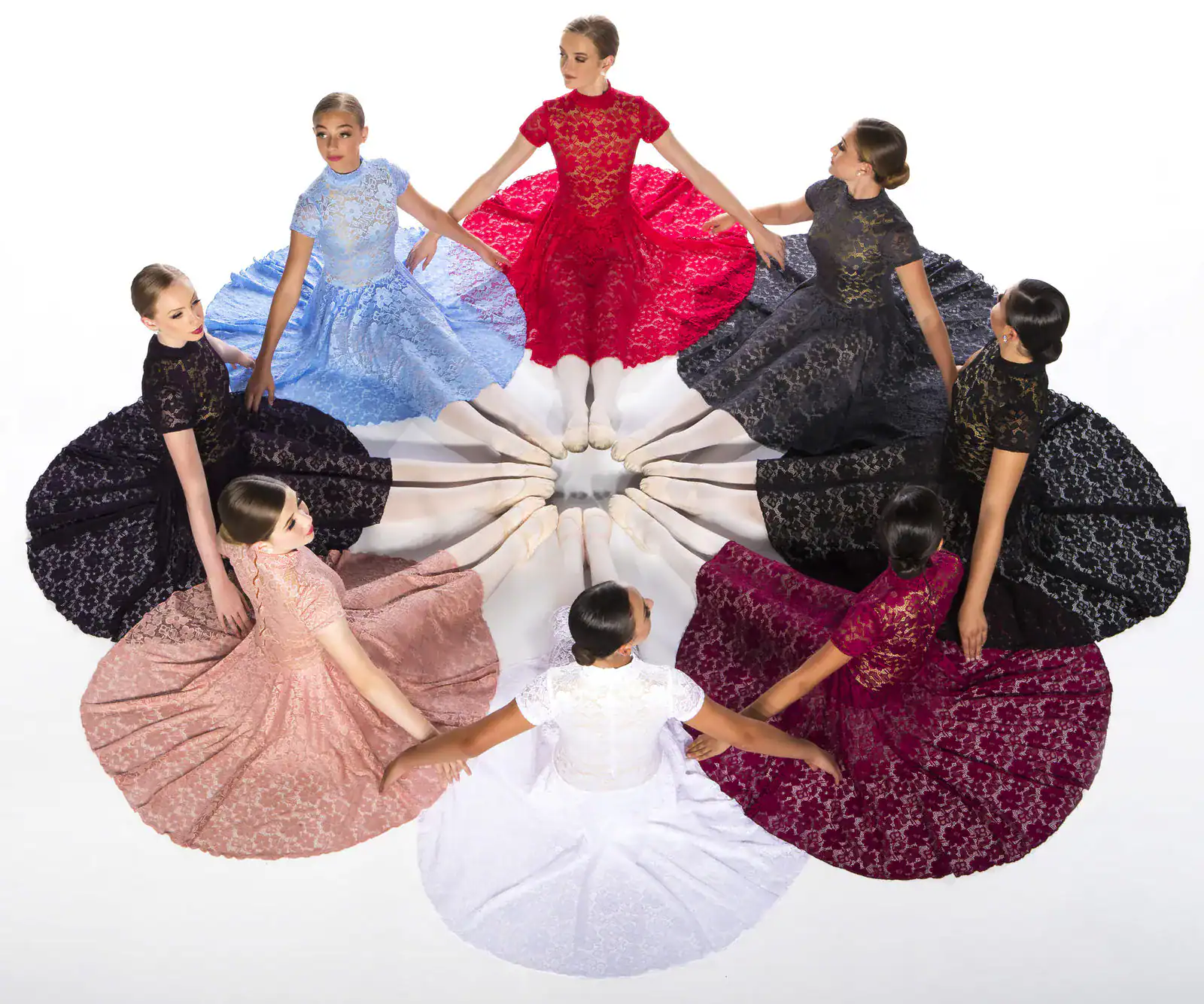 Ballerinas seated in a circle wearing colorful lace dresses