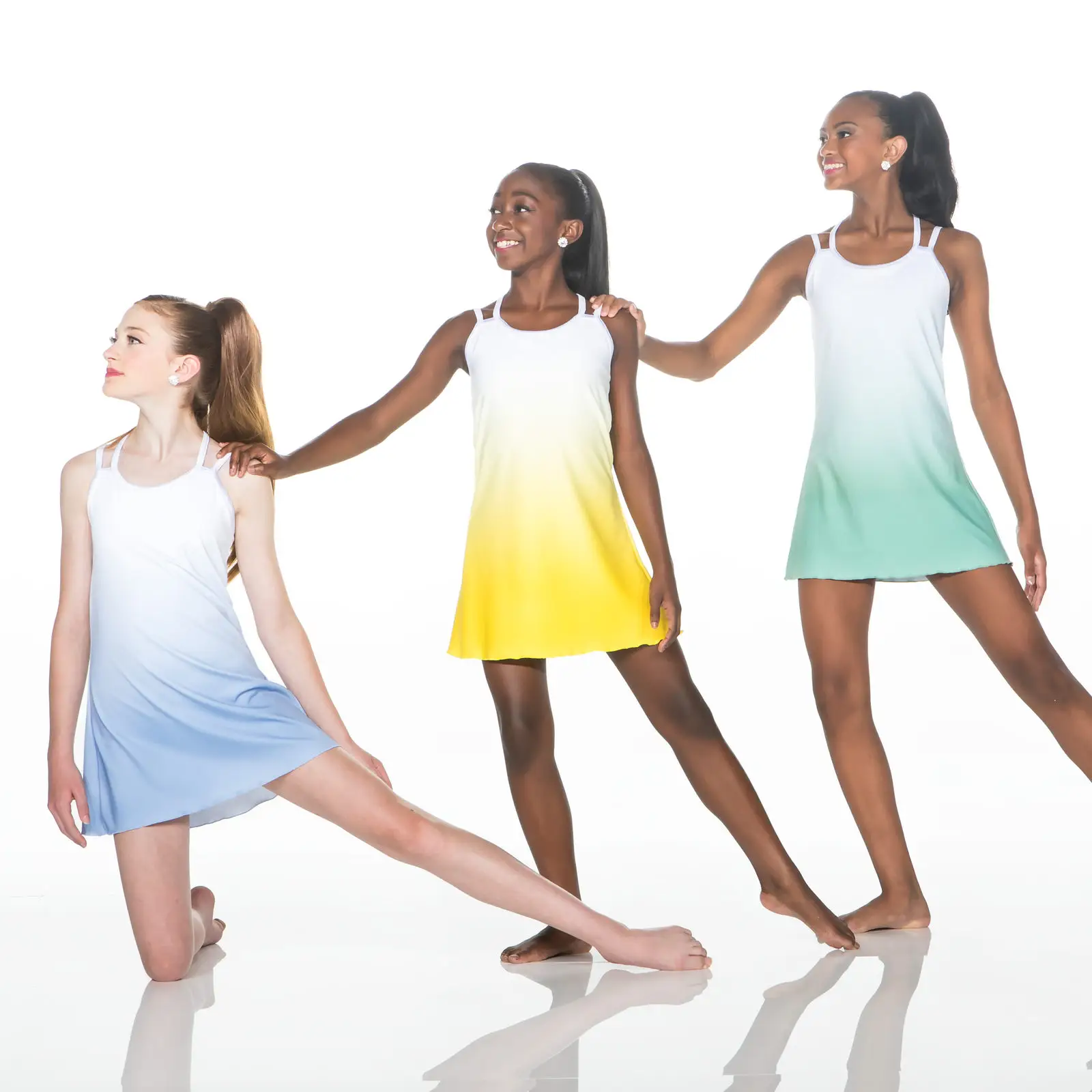 Three dancers wearing pastel gradient dresses pose together.