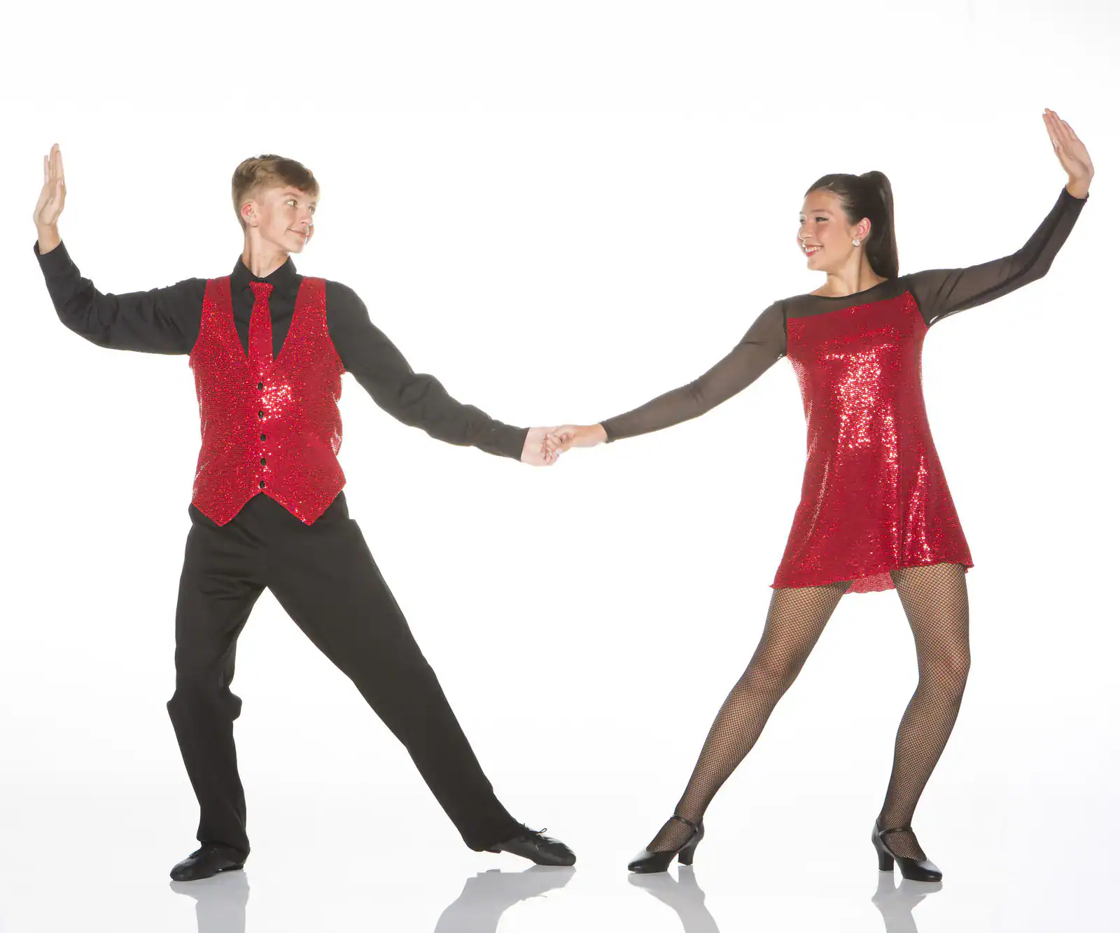 Two dancers in red sequins hold hands in pose.