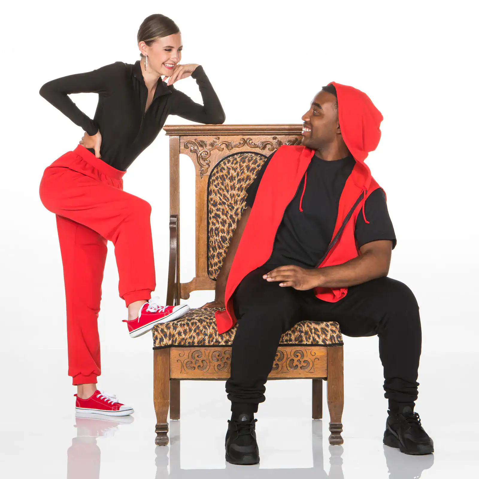 Two people in red and black outfits pose with ornate chair.